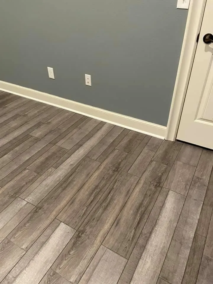 Gray plank flooring meeting a blue gray wall with clean baseboard